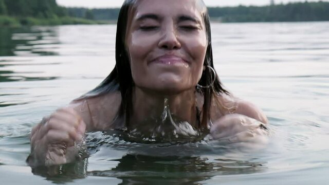 closeup on sexy seductive young woman who dives into lake, then pops up from water. attractive asian fit female with long hair in swimsuit swimming. summer chill, vacation, rest , fun, joy at nature