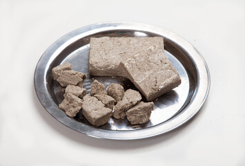 Halva in briquettes and in large pieces lies on a metal plate on a white background.
