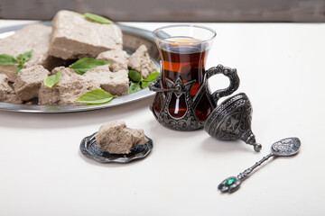 Turetius a glass of tea, a metal spoon and sunflower halva with almonds and pistachios stands on a wooden background.