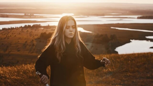 Young woman in black clothes training with a sword while sunset on nature