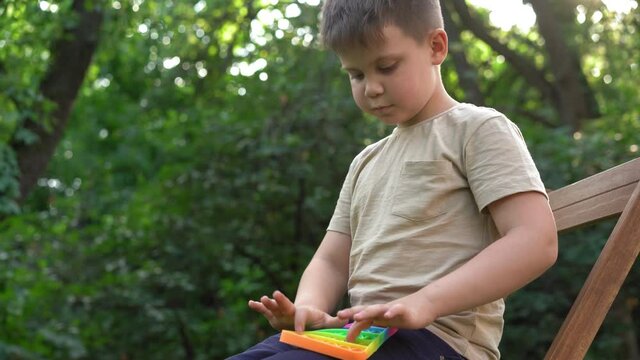 Kid Holding Rainbow Pop It Fidget Toy in Garden. Child is Playing Trendy Popular Board Game Anti-Stress Toy Pop It (Popit or Simple Dimple). Jule 2020. Kyiv, Ukraine. High quality 4k footage