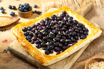 Puff pastry pie with cottage cheese and blueberries on a serving board on the culinary table