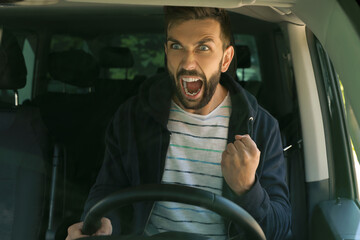 Stressed angry man in driver's seat of modern car, view through windshield
