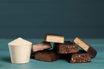 Pieces of tasty bars and cup with protein powder on light blue wooden table. Space for text
