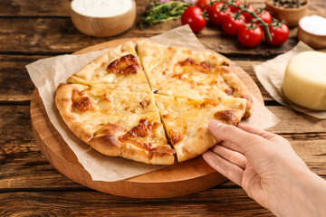 Woman taking piece of delicious khachapuri with cheese at wooden table, closeup