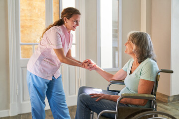 Pflegedienst Frau hält Hand von Seniorin im Rollstuhl