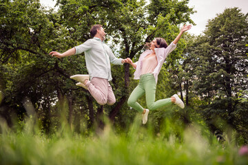 Photo of shiny carefree couple wear casual clothes smiling holding arms jumping high outdoors urban...