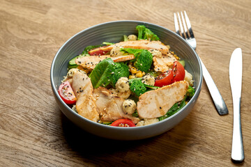 Diet salad with chicken, broccoli and cherry tomatoes in a bowl on a wooden background. Close up, selective focus