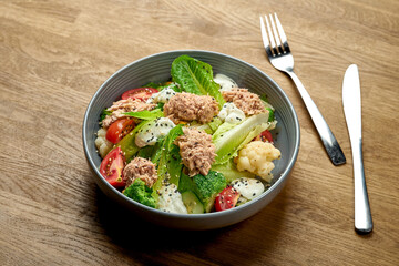 Diet salad with tuna, broccoli and cherry tomatoes in a bowl on a wooden background