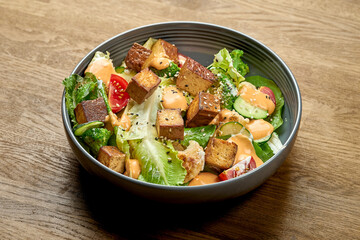 Diet salad with fried tofu, yellow sauce and vegetables in a bowl on a wooden background