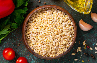 Dry uncooked pearl barley in a wooden bowl on a dark background close-up. 