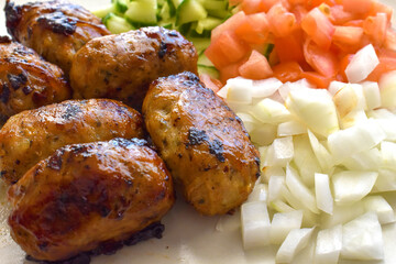 Sheftalia : Cypriot Lamb and Pork Sausages. Grilled Sausages with Fresh Vegetables (Cucumber, Tomato and Onion) on a White Plate. Traditional Cypriot food.	
