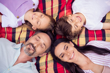 Photo of pretty adorable family dressed casual outfit lying checkered blanket closed eyes smiling outside urban city street