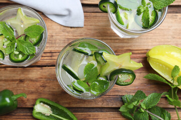 Glasses of spicy cocktail with jalapeno, carambola and mint on wooden table, flat lay
