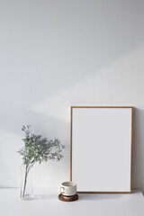 Wooden empty picture frame and flowers on white wall.