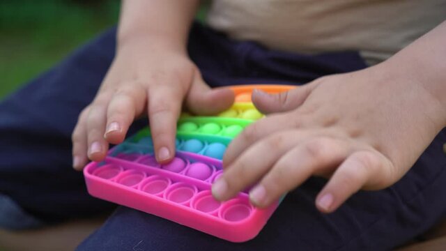 Kid Holding Rainbow Pop It Fidget Toy in hands. Child is Playing Trendy Popular Board Game Anti-Stress Toy Pop It (Popit or Simple Dimple). Jule 2020. Kyiv, Ukraine. High quality 4k footage