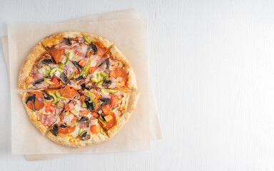 Top view of hot delicious traditional italian whole pizza with tomatoes, mushrooms, meat and cheese  sliced and served on white wooden background on craft paper. Image with copy space, horizontal