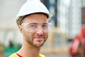 Pleased attractive builder in safety goggles posing for the camera