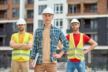 Three men in protective helmets standing on the building site