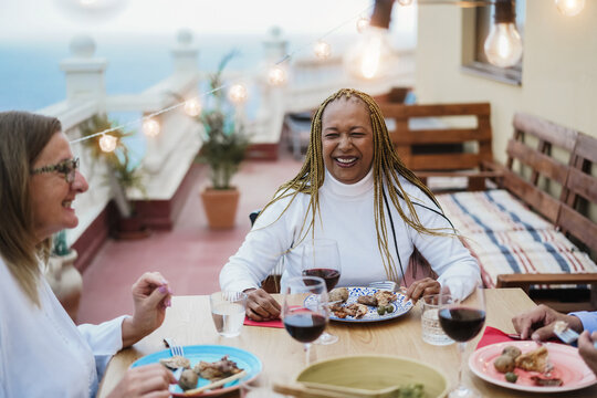 Senior People Having Fun Eating And Drinking Wine At Patio Dinner - Focus On African American Woman Face