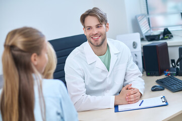Fototapeta premium Cheerful pediatric audiologist sitting at the desk during the consultation