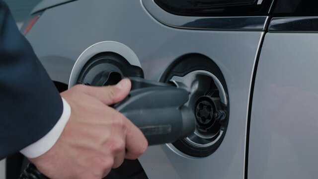 Male hands unplugs the electric vehicle and close the lid. Electric vehicle charging technology concept. Businessman disconnects the charging plug wire from the hybrid car