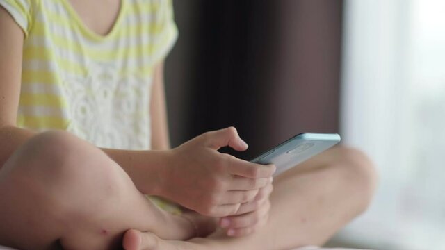 Little girl using mobile phone at home. Close up child hands with smartphone pressing finger, reading social media internet, chatting, typing text or shopping online. Mobile phone in two hands
