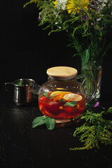 Glass transparent teapot with fruit on a dark background