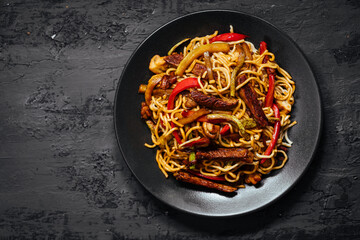 Wok with turkey meat, noodles, paprika, mushrooms and carrot served on a black background with...
