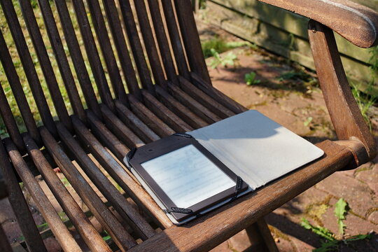 E-ink ebook reader lying on a wooden chair in the garden 
