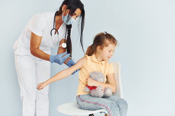 Little girl with teddy bear. Doctor in uniform making vaccination to the patient