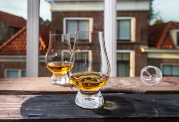 Dram of single malt scotch whisky served in tasting glass with view on old window and houses