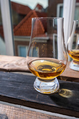 Dram of single malt scotch whisky served in tasting glass with view on old window and houses