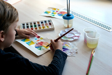 Boy painting pictures with watercolor paints during art lesson online
