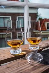 Dram of single malt scotch whisky served in tasting glass with view on old window and houses