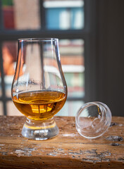 Dram of single malt scotch whisky served in tasting glass with view on old window and houses