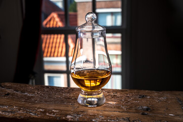 Dram of single malt scotch whisky served in tasting glass with view on old window and houses