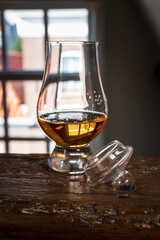 Dram of single malt scotch whisky served in tasting glass with view on old window and houses