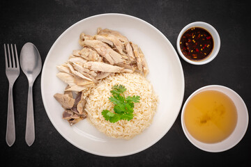 Khao Mun Gai, Thai food, rice steamed with chicken soup serve with chicken, soup and sauce on dark tone texture background, top view