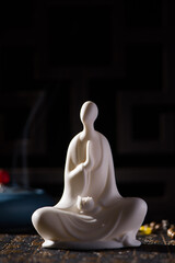 A small white Buddha figure sits with burner censer on black background