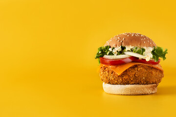 Crispy chicken burger with cheese on yellow background.Copy space