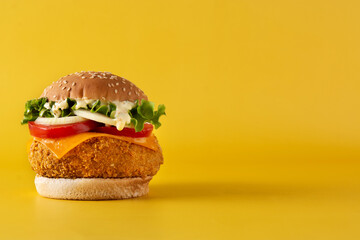 Crispy chicken burger with cheese on yellow background.Copy space