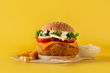 Crispy chicken burger with cheese on yellow background