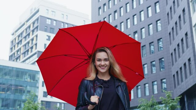 A young woman in black clothes walks around the city with a red umbrella. A modern residential area in the background