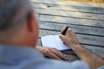 old man writing his ideas in a blank notepad outdoor close up