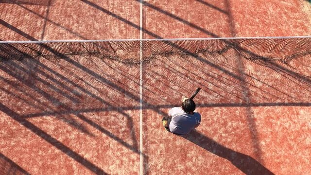 Overhead shot of a person practicing paddle tennis techniques on an outdoor court. He is constantly hits the ball with the racket.