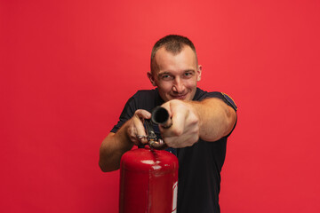 Fire safety. Portrait of young smiling man with extinguisher posing over red background.