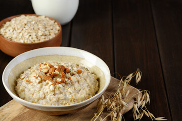 A bowl of oatmeal porridge with almonds next to some ears of oats on the table. Copy space. Healthy eating, vegan and vegetarian food.