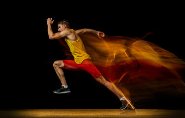 Portrait of young man, professional male athlete, runner in motion and action isolated on dark...