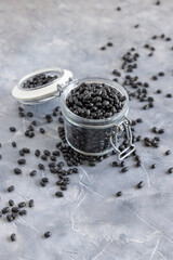 Fototapeta na wymiar Glass jar full of dry black beans on grey table